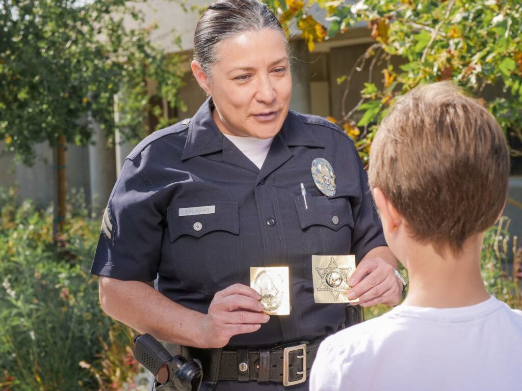 Friendly police officer showing badges to a child outdoors in a community setting.