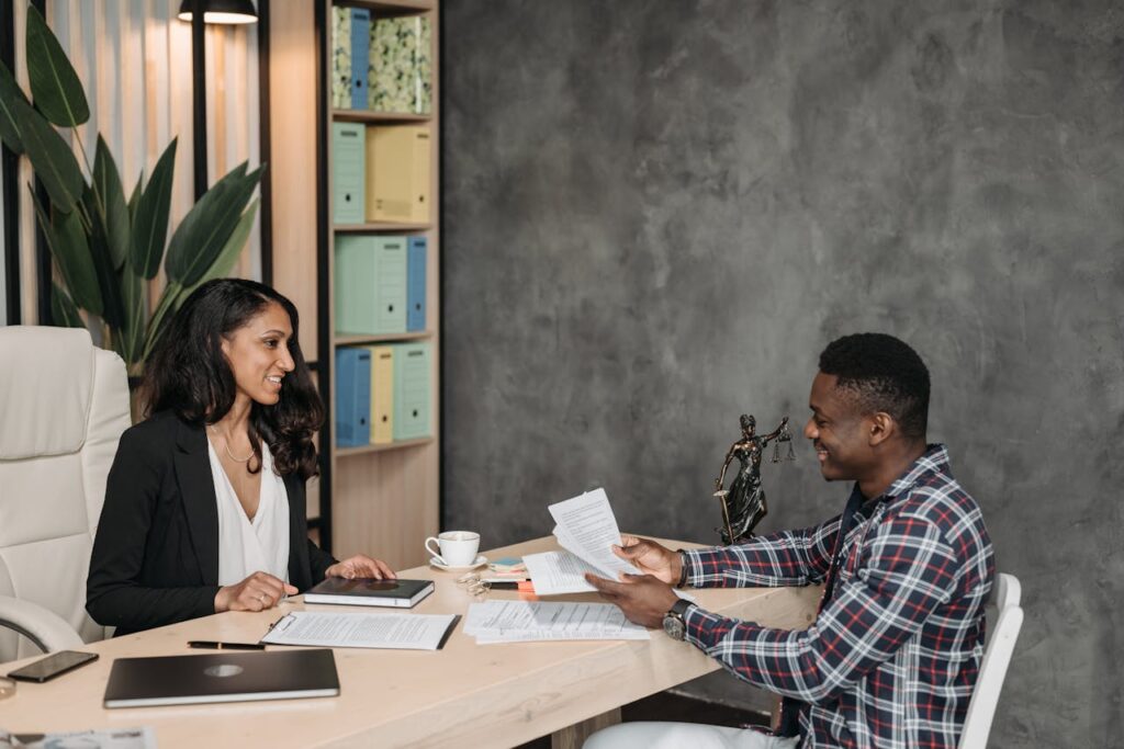 Two professionals having a discussion in a stylish office with paperwork and a laptop.